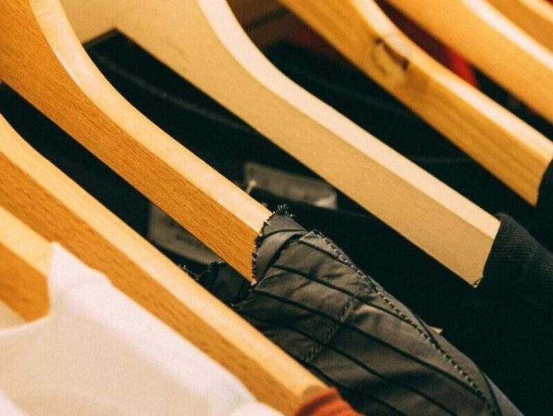 A close-up view of a row of clothes on wooden hangers, showcasing various fabrics and colors in a wardrobe setting.